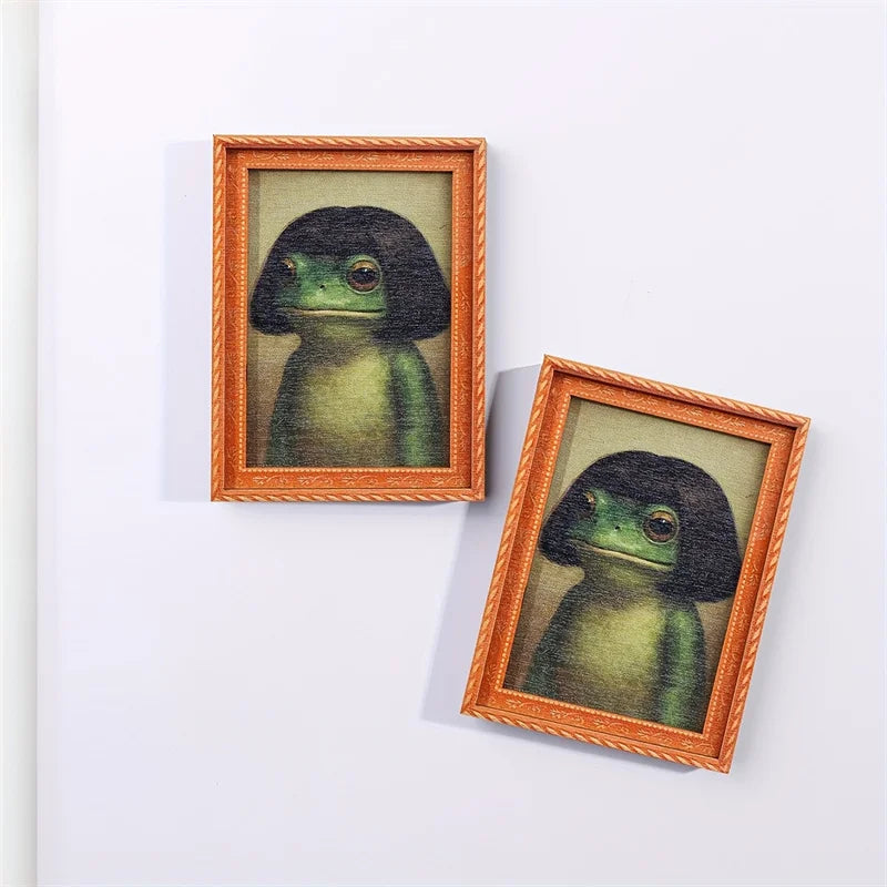 A framed illustration of a green frog in a wooden frame with a braided border.