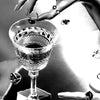 A hand holds a cut crystal glass with a dark liquid, set against a bright background.