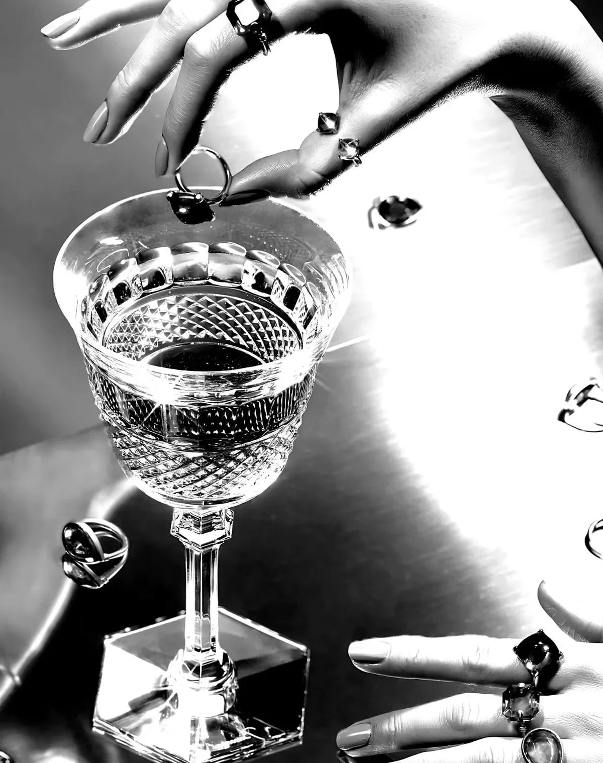 A hand holds a cut crystal glass with a dark liquid, set against a bright background.