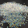 A pile of iridescent nail rhinestones scattered on a dark surface.