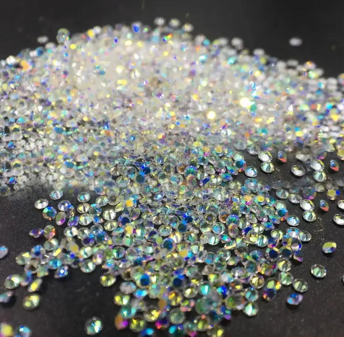 A pile of iridescent nail rhinestones scattered on a dark surface.