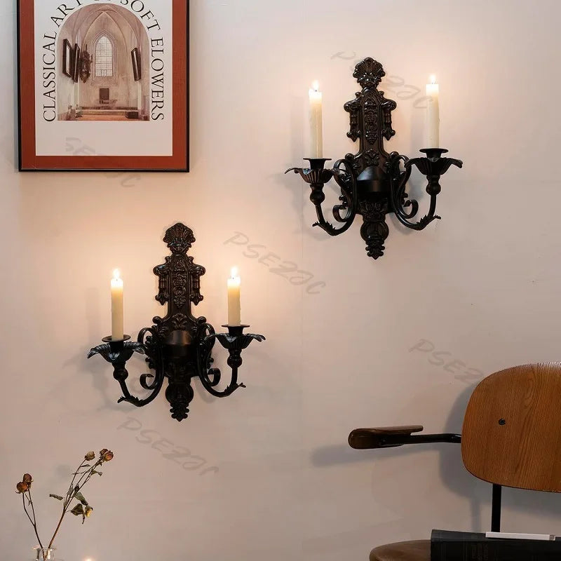 A vintage black wall pendant candle holder with multiple arms and candlesticks mounted on a white wall.