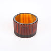 A cylindrical glass candle holder with a ribbed texture, featuring an amber or gold tint and a dark rim.
