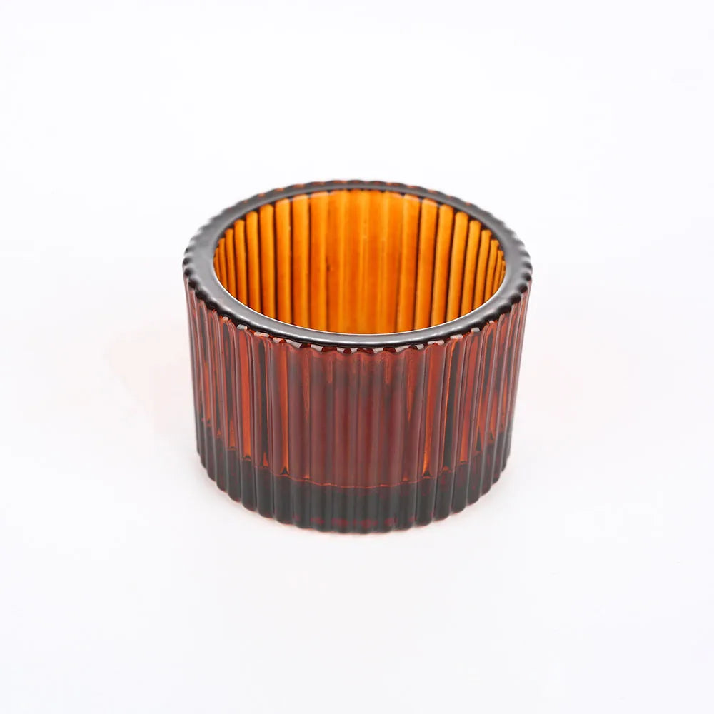 A cylindrical glass candle holder with a ribbed texture, featuring an amber or gold tint and a dark rim.