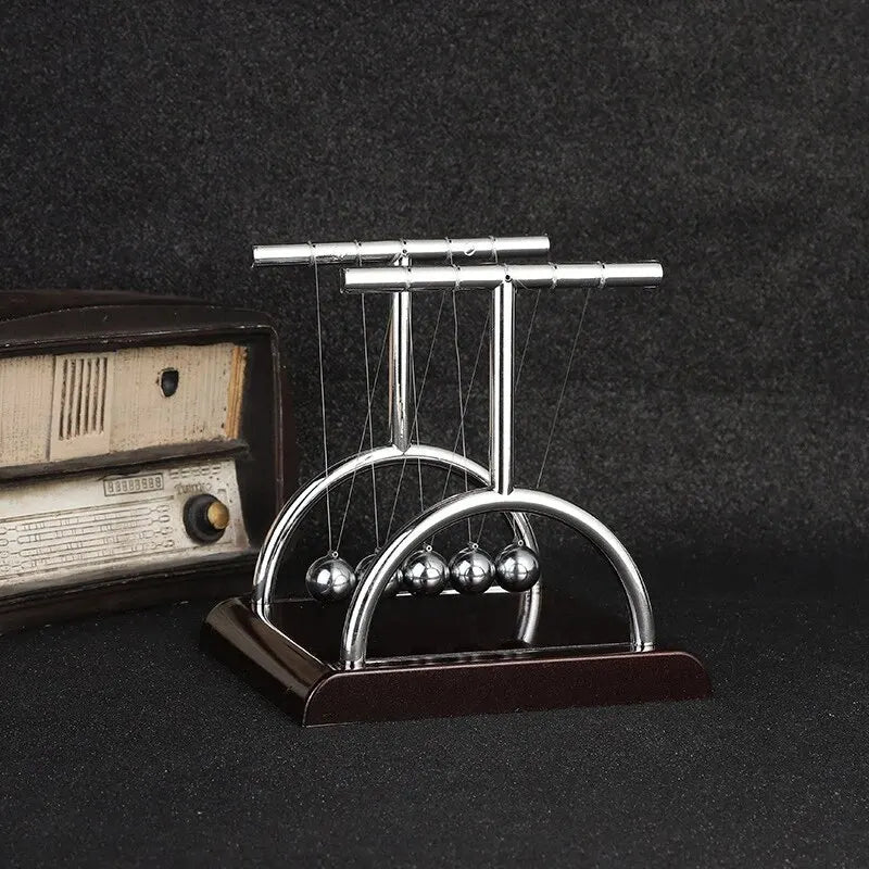 A silver Newton's cradle with balance balls on a dark wooden base.