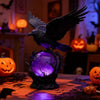 A dark raven sculpture with purple LED glow sits on a wooden surface in a dimly lit setting.