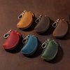 A collection of six brown and green leather key pouches with carabiner clips arranged on a dark surface.