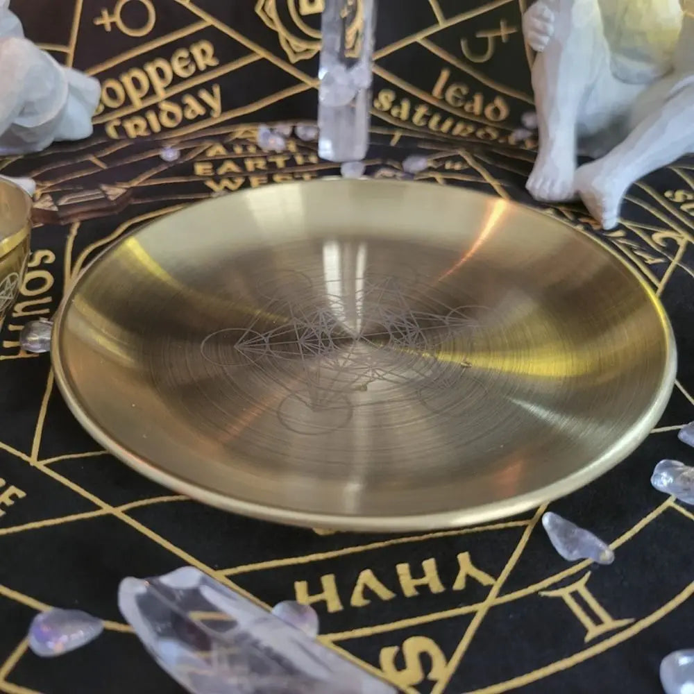 A round, polished brass or gold-toned stainless steel altar plate with a pentagram design resting on a dark surface.