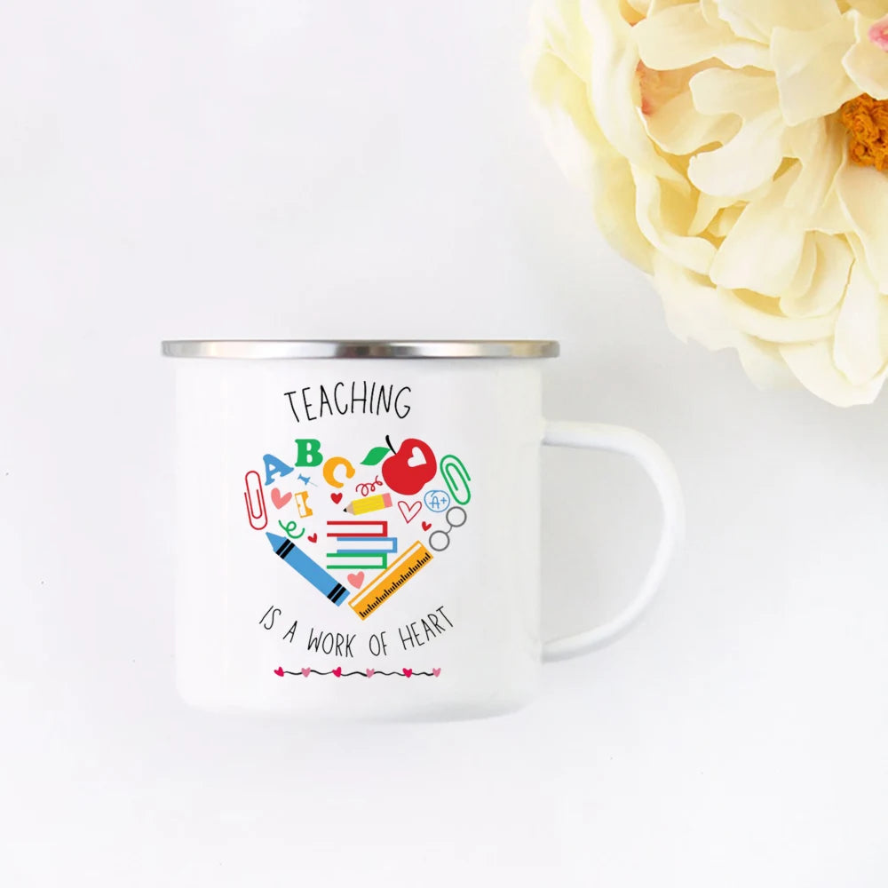 A white enamel mug with a design that reads Teaching is a work of heart and features colorful letters and a heart.