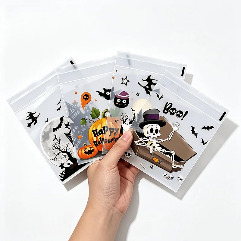 A hand holds several clear self-adhesive treat bags decorated with Halloween themes like bats skulls and pumpkins.