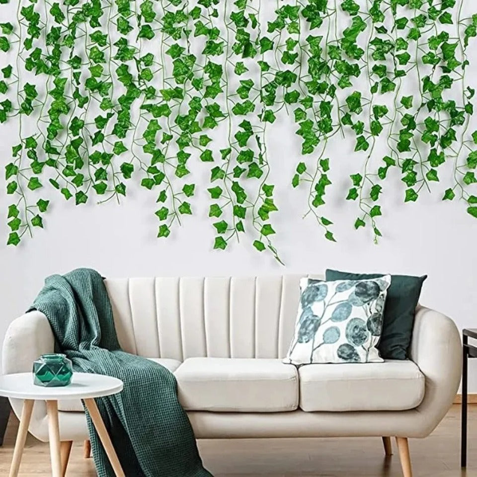 Artificial ivy vine garland draped across a white wall, decorating a light-colored sofa and surrounding area.