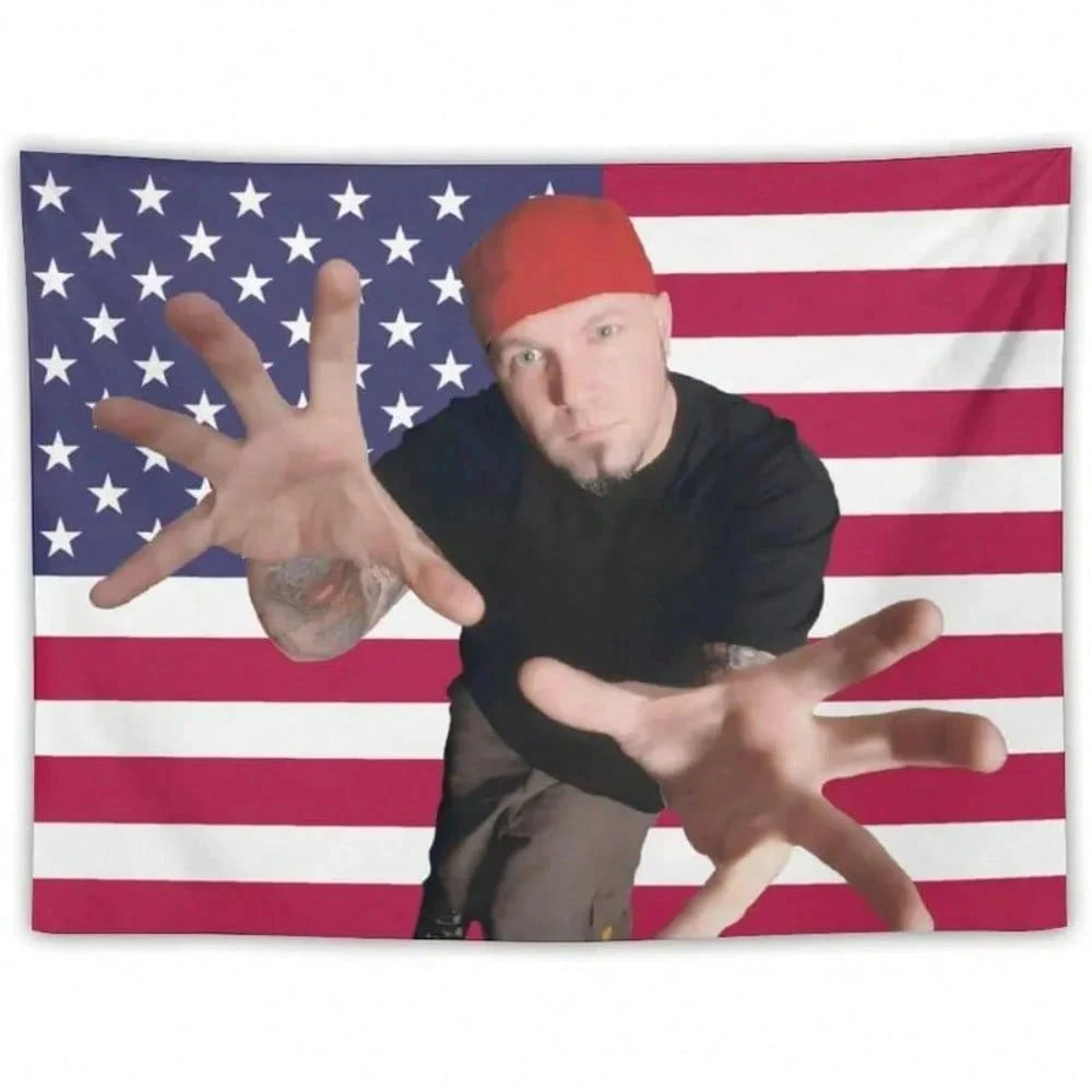 A man wearing a red cap stands in front of an American flag background with his hands outstretched.