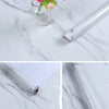 Roll of self-adhesive marble contact paper shown on a white marble surface with a glass vase and pink flower.