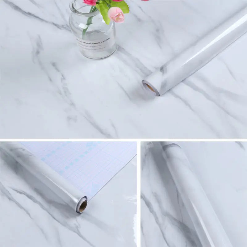 Roll of self-adhesive marble contact paper shown on a white marble surface with a glass vase and pink flower.