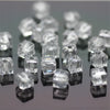 A collection of clear square cut glass crystal beads for jewelry making displayed on a dark surface.