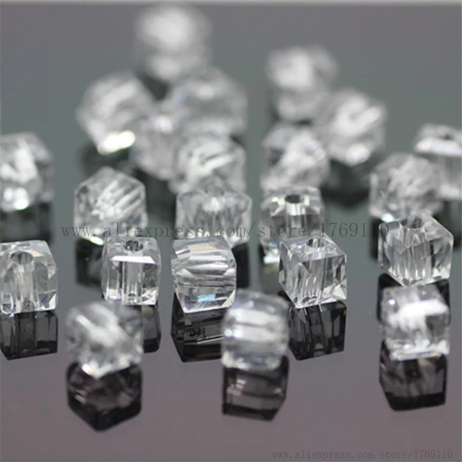 A collection of clear square cut glass crystal beads for jewelry making displayed on a dark surface.