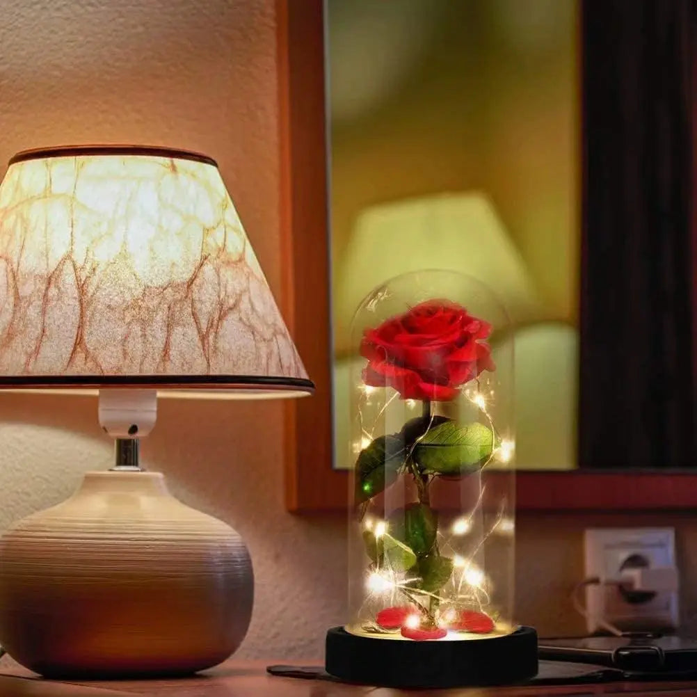 A glass jar containing a red rose and glowing wire lights simulating an eternal flower.