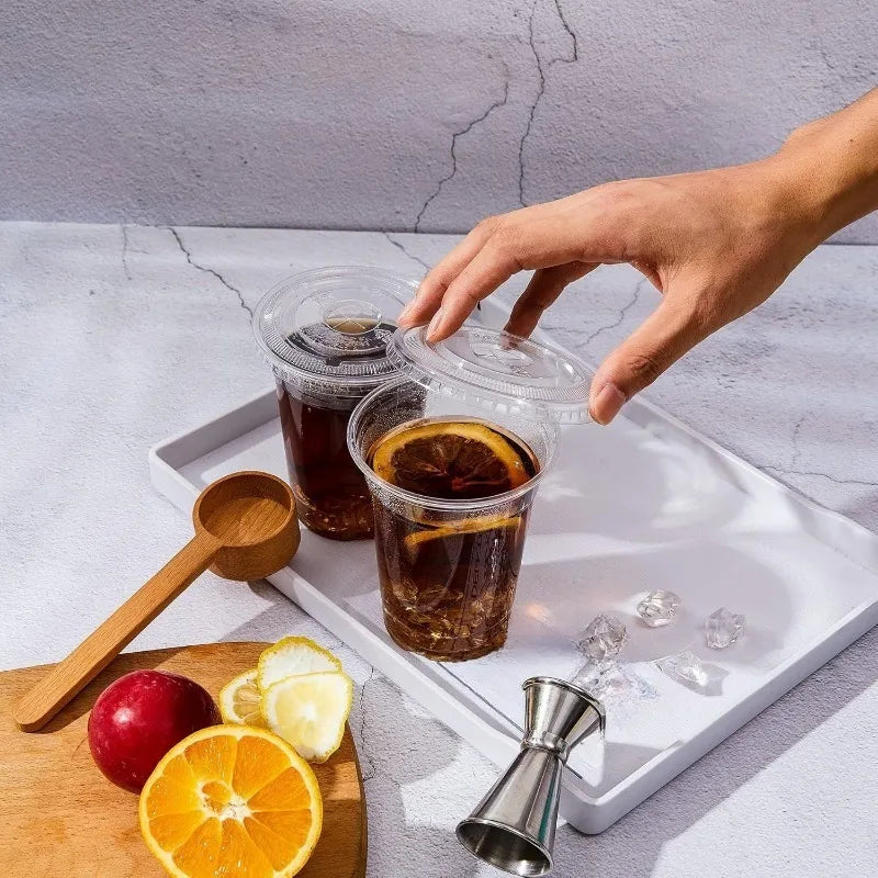 A hand is holding a disposable plastic cup with a lid containing iced tea on a white tray.