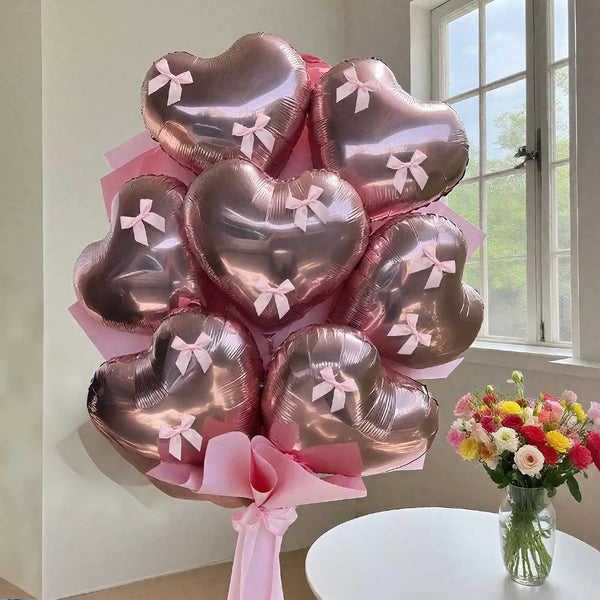 A bouquet of pink heart-shaped foil balloons tied with ribbons, displayed on a white table.