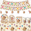 A collection of happy capybara themed birthday party decorations including banners, cupcake toppers, and themed food items.