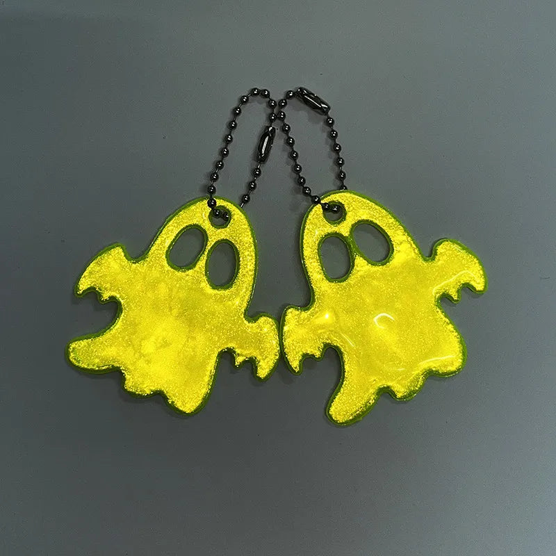 A set of two yellow ghost-shaped reflective keychains with black cords.