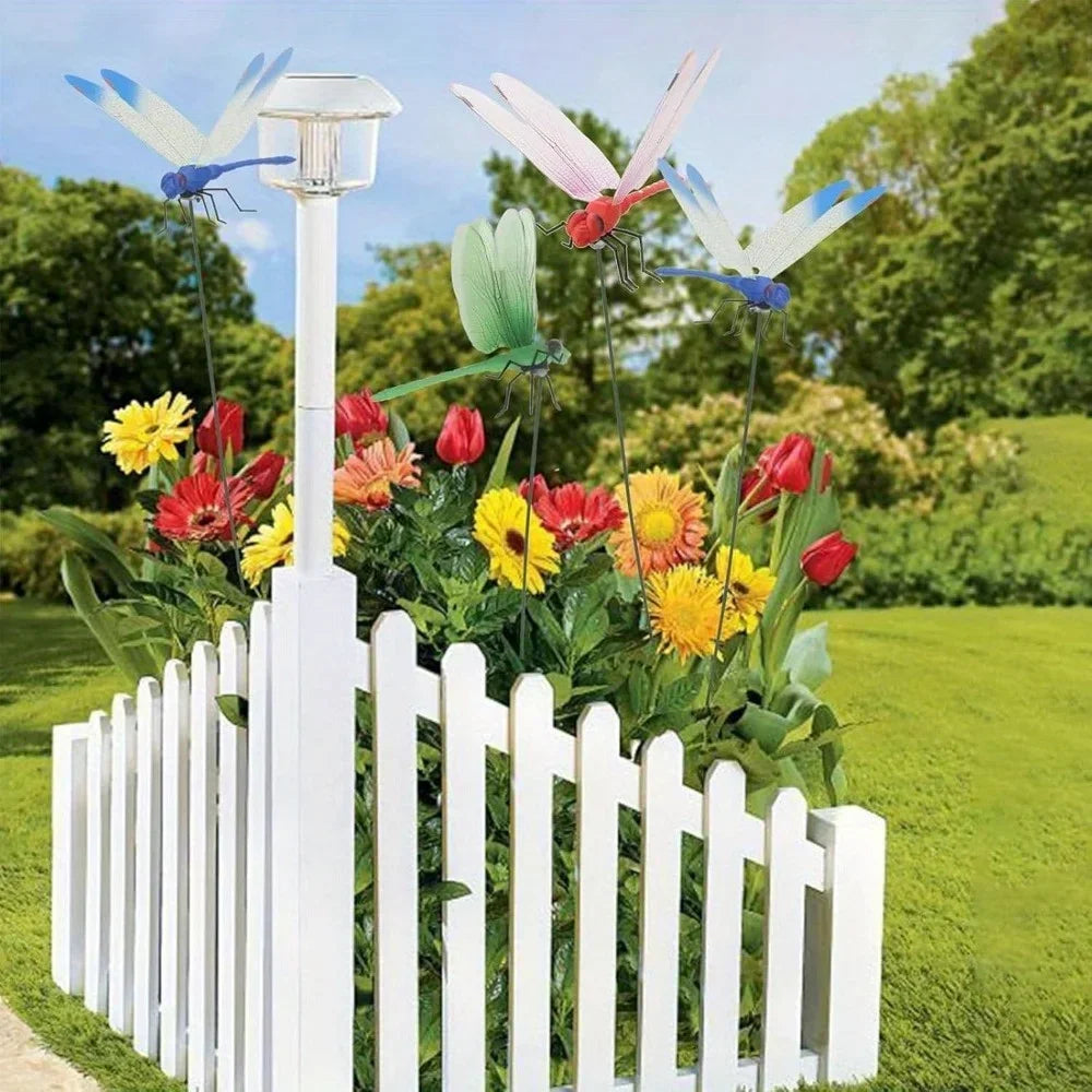 White picket fence decorated with realistic dragonfly hat clips and colorful garden flowers.
