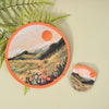 A round, orange handheld cooling fan featuring a landscape painting with mountains and a setting sun.