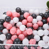 A large plastic basket filled with a variety of pink, white, and black spherical balls for play.