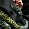 A hand holds a dark green 3D printed rotatable snake art model with gold eyes against a black background.
