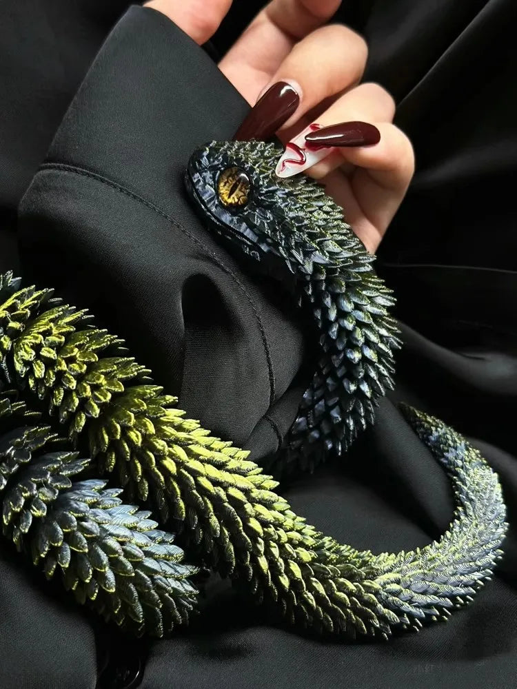 A hand holds a dark green 3D printed rotatable snake art model with gold eyes against a black background.