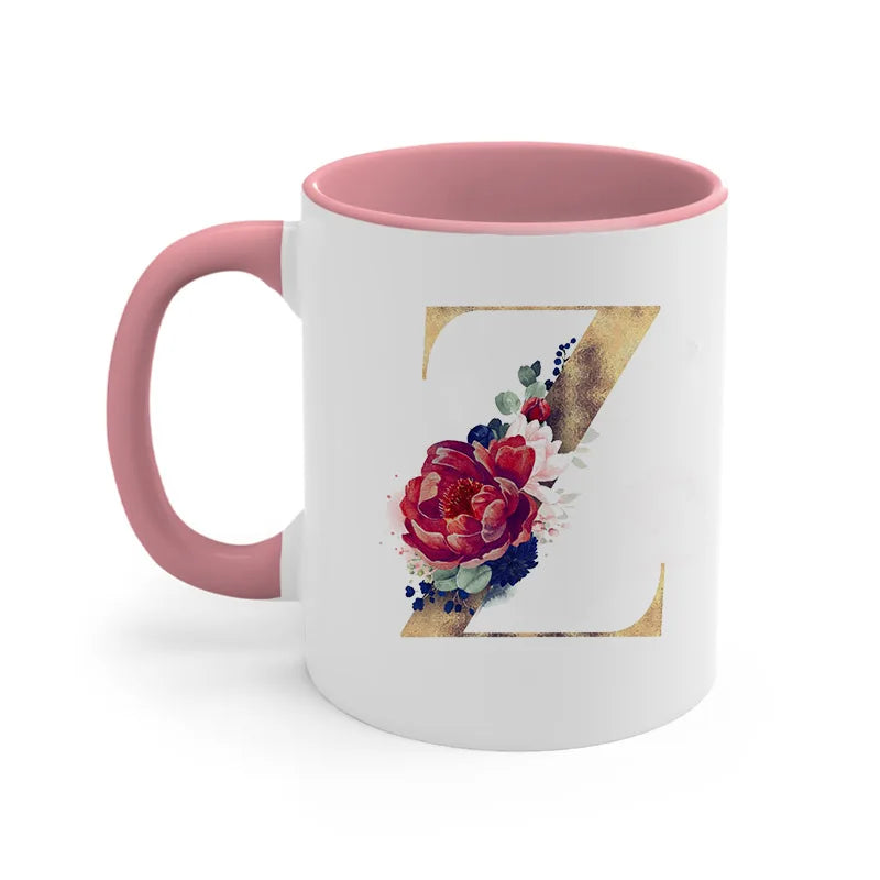 A pink ceramic coffee mug featuring a gold letter Z design with floral accents.