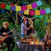 A group of people enjoying an outdoor evening with colorful papel picado banners strung across the scene.