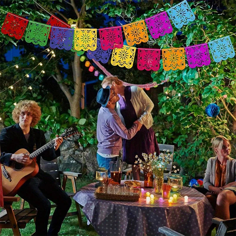 A group of people enjoying an outdoor evening with colorful papel picado banners strung across the scene.
