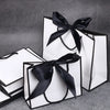 A set of five elegant black and white gift bags tied with black ribbon bows on a gray surface.