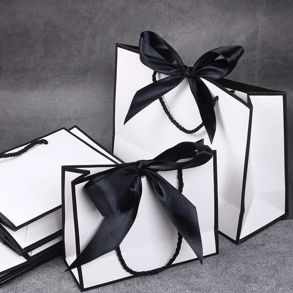 A set of five elegant black and white gift bags tied with black ribbon bows on a gray surface.