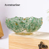 A clear green Aventurine bowl with a lotus design sits on a light wooden block.