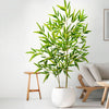 Artificial bamboo branch with green leaves in a white pot displayed indoors.