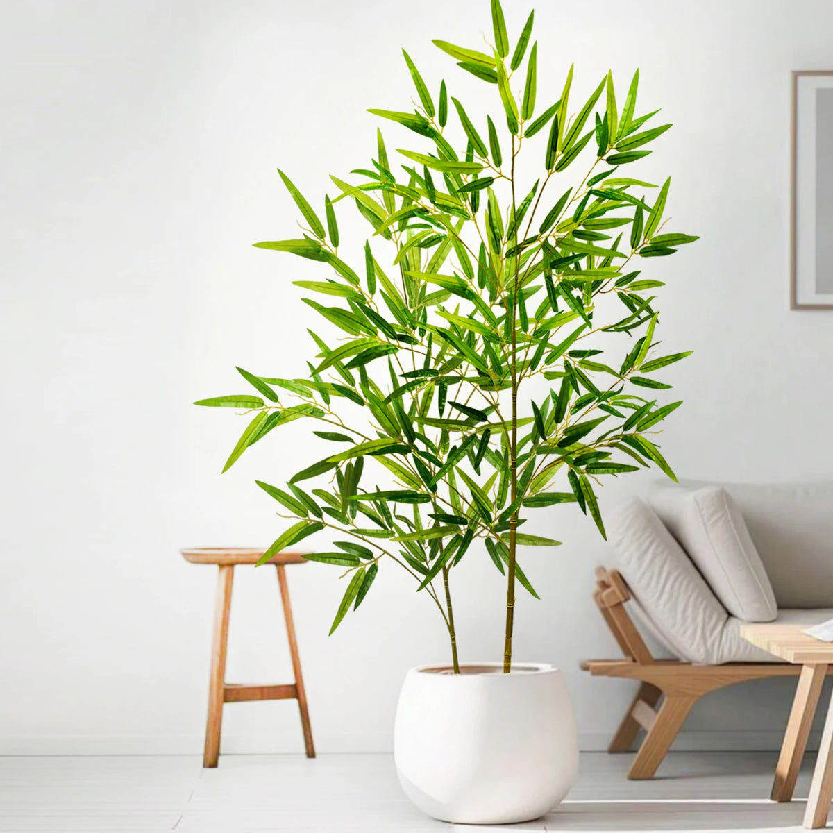 Artificial bamboo branch with green leaves in a white pot displayed indoors.