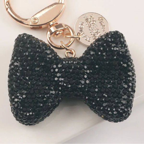 A black sparkling rhinestone bow keychain with a gold-toned clasp and circular tag.