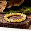 A round bracelet made of yellow citrine crystal beads resting on a rustic wooden surface with moss and leaves in the backgrou