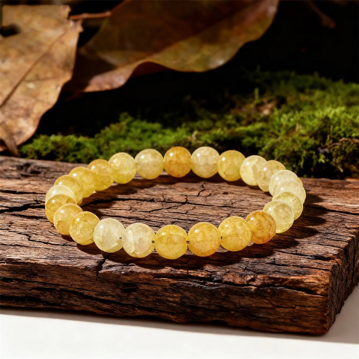 A round bracelet made of yellow citrine crystal beads resting on a rustic wooden surface with moss and leaves in the backgrou