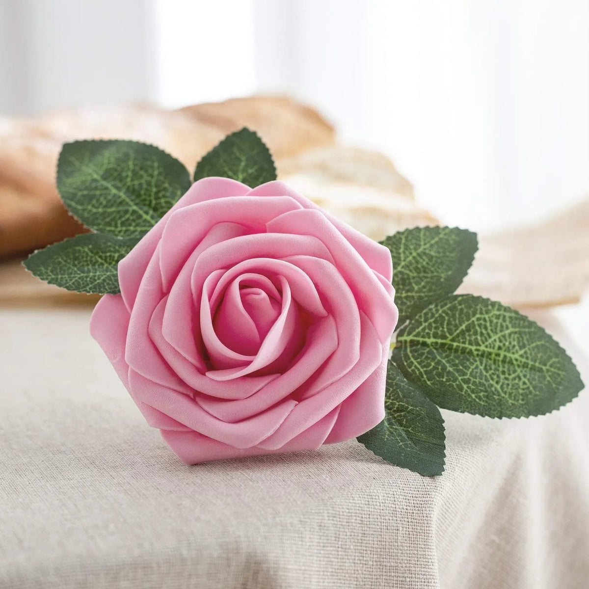 A pink foam rose with green leaves resting on a light fabric.