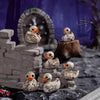 A collection of resin skull duck figurines displayed on a dark, rocky surface with a stone archway background.