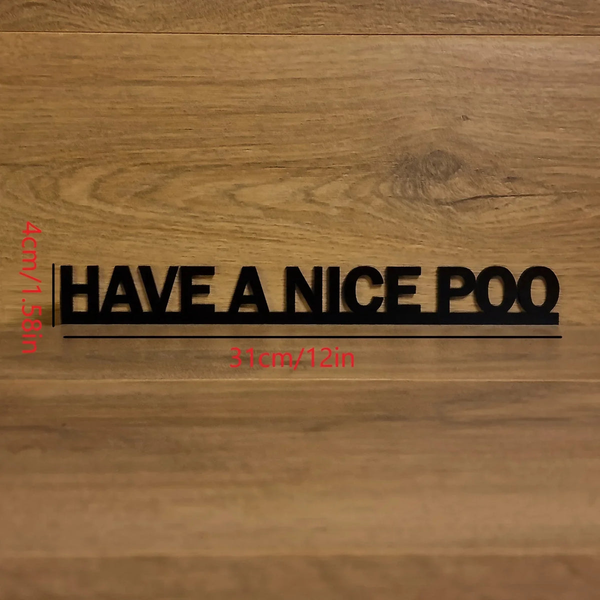A black acrylic sign with the text HAVE A NICE POO is mounted on a wooden surface.