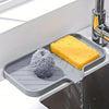 A silicone faucet splash guard and drying mat placed in a kitchen sink, with water dripping onto the mat.