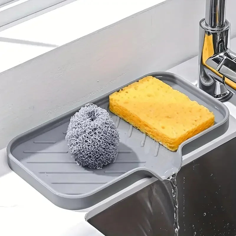 A silicone faucet splash guard and drying mat placed in a kitchen sink, with water dripping onto the mat.