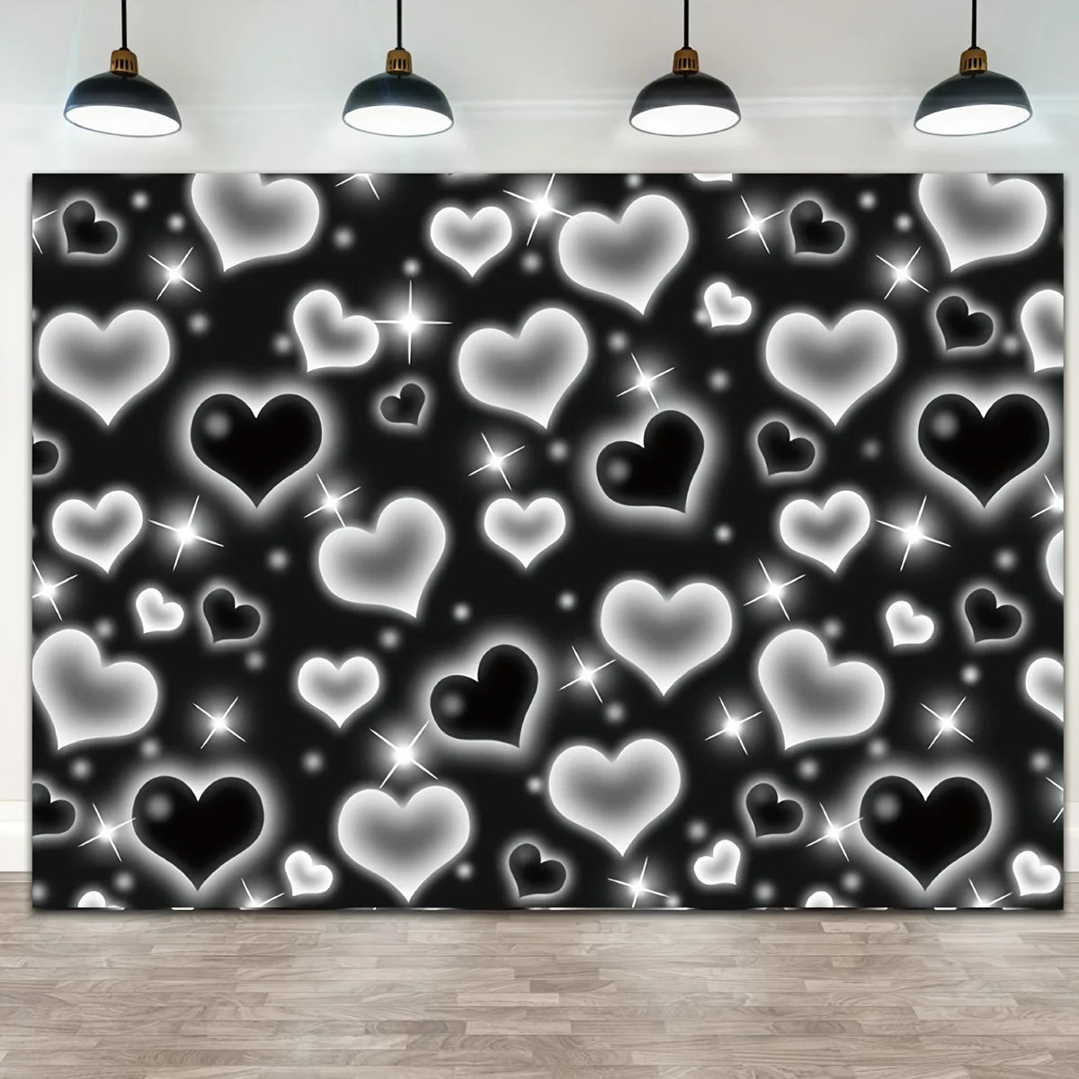 A black backdrop covered in silver and white glittering heart shapes, lit by overhead pendant lights.