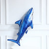 A blue foil balloon shaped like a shark is displayed against a white framed background.