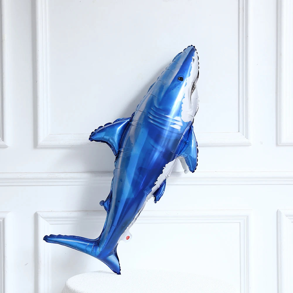 A blue foil balloon shaped like a shark is displayed against a white framed background.