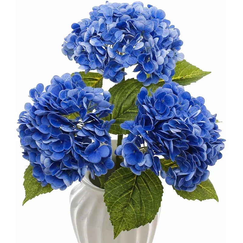 A bouquet of large, vibrant blue artificial hydrangea flowers in a white vase.